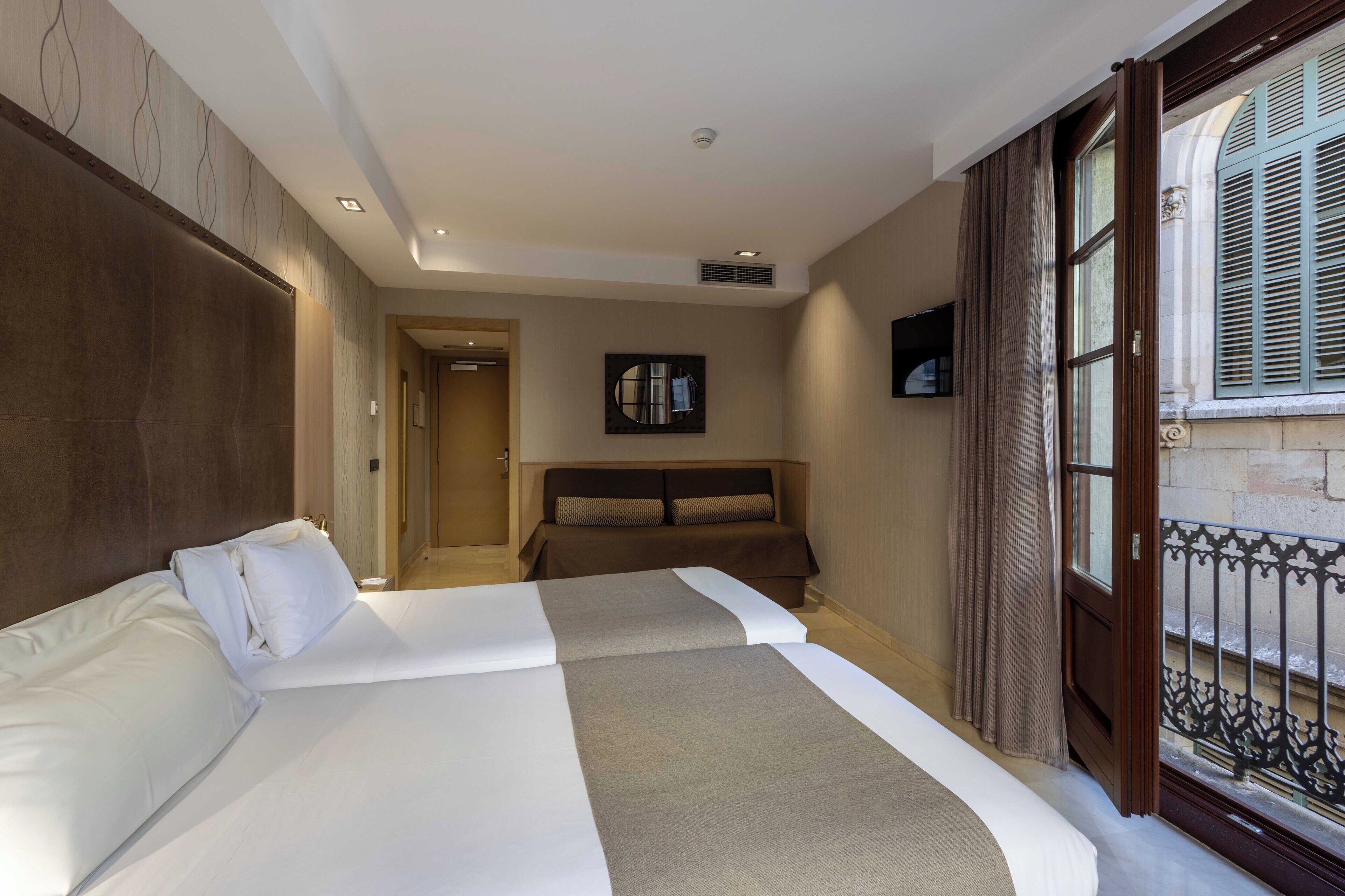 Ein Hotelzimmer mit zwei Betten, einem großen Spiegel und Blick auf die Straße durch ein Fenster mit Rollläden.