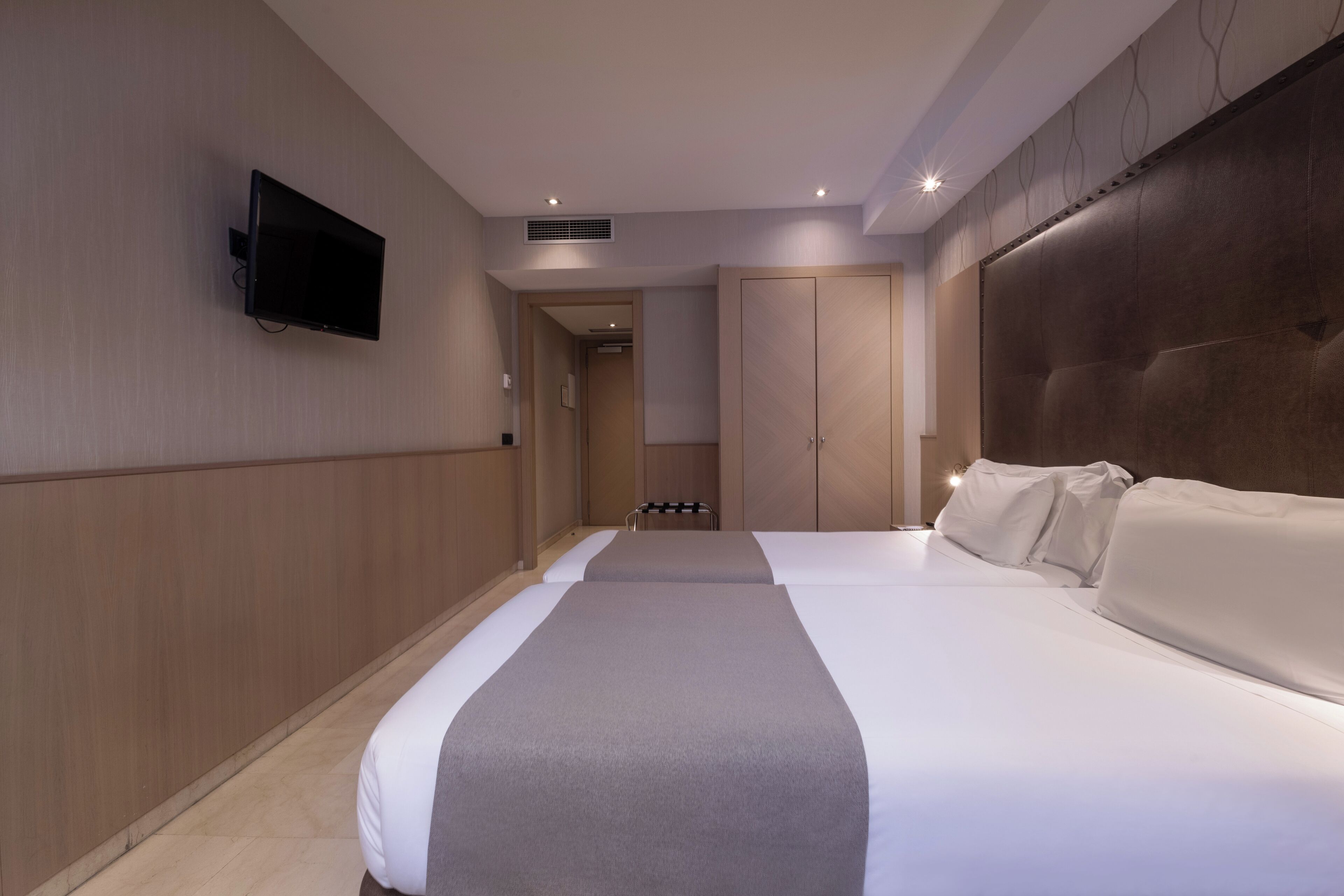 A hotel room with two beds, a flat-screen TV mounted on the wall, and a large wardrobe.