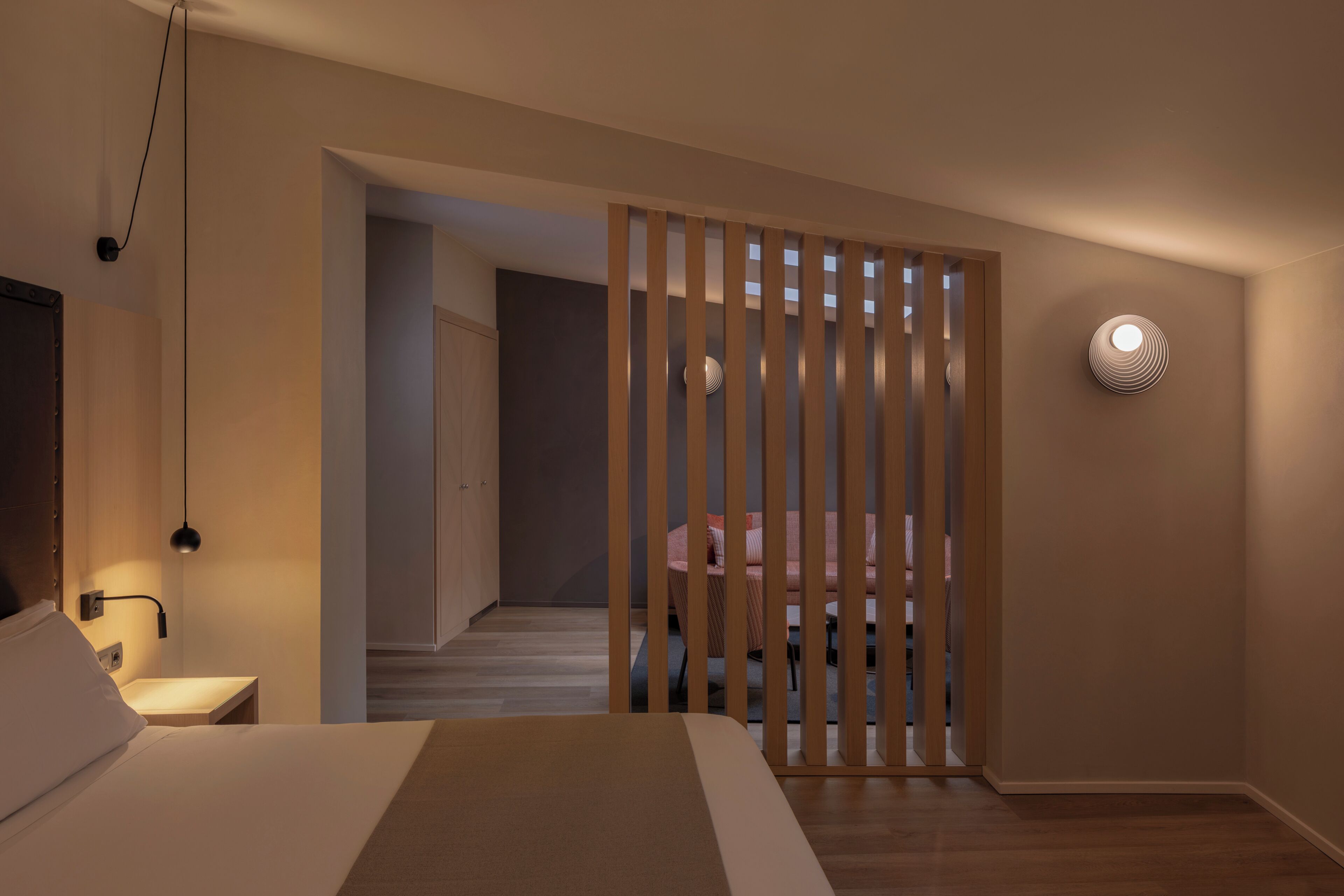 Een slaapkamer met een bed, nachtkastje, lamp en uitzicht door een houten scheiding op een trap en een andere kamer.