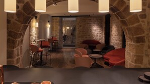 A restaurant with stone walls, red and black upholstered seating, and pendant lighting. - Gran Hotel Barcino (Barcelona)