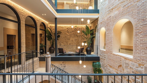 A multi-level atrium with stone walls, a staircase, and hanging lights. - Gran Hotel Barcino (Barcelona)