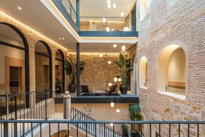 Ein mehrgeschossiges Atrium mit Steinwänden, einer Treppe und hängenden Leuchten.