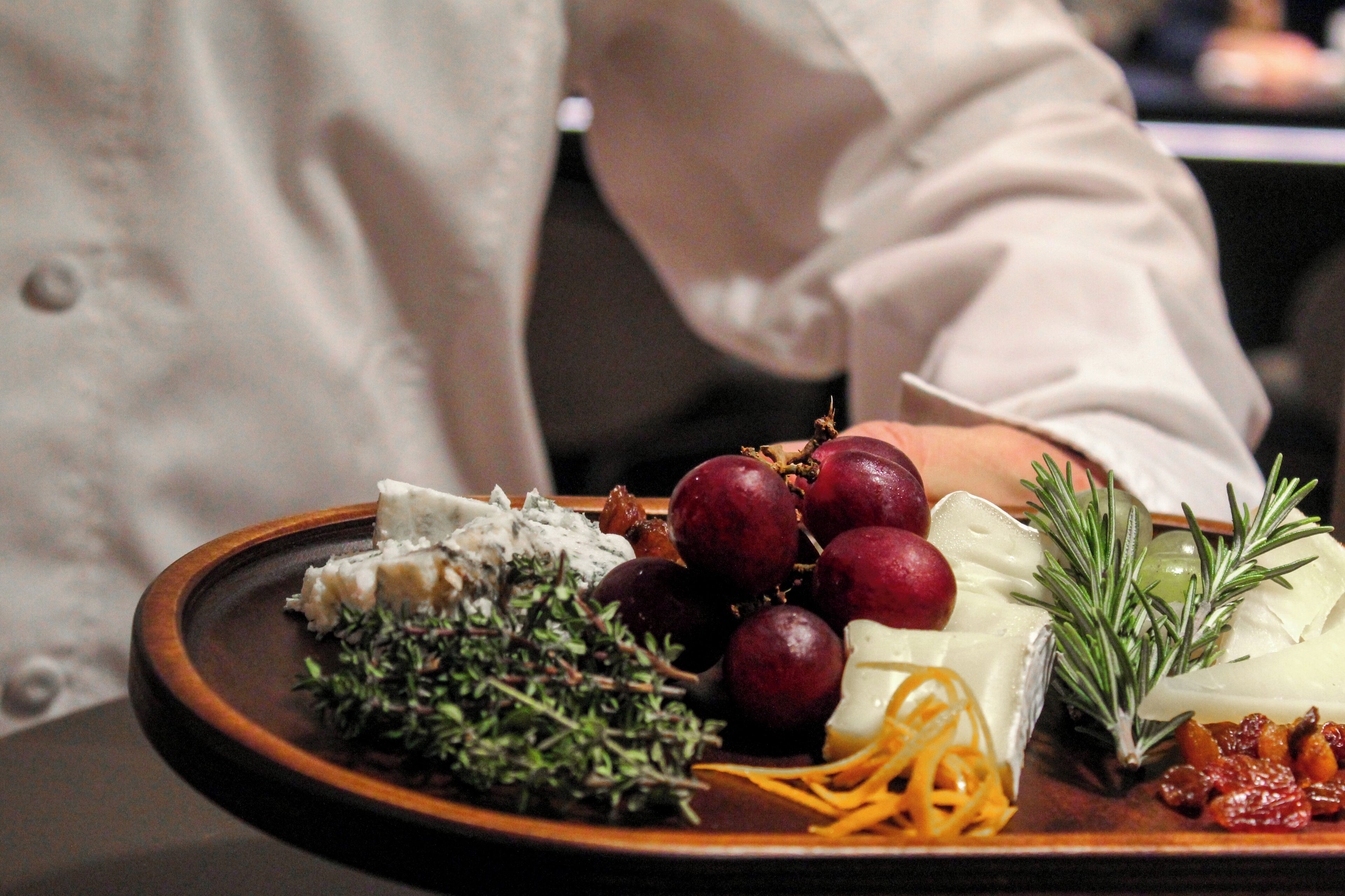 A plate with various cheeses, grapes, and herbs.