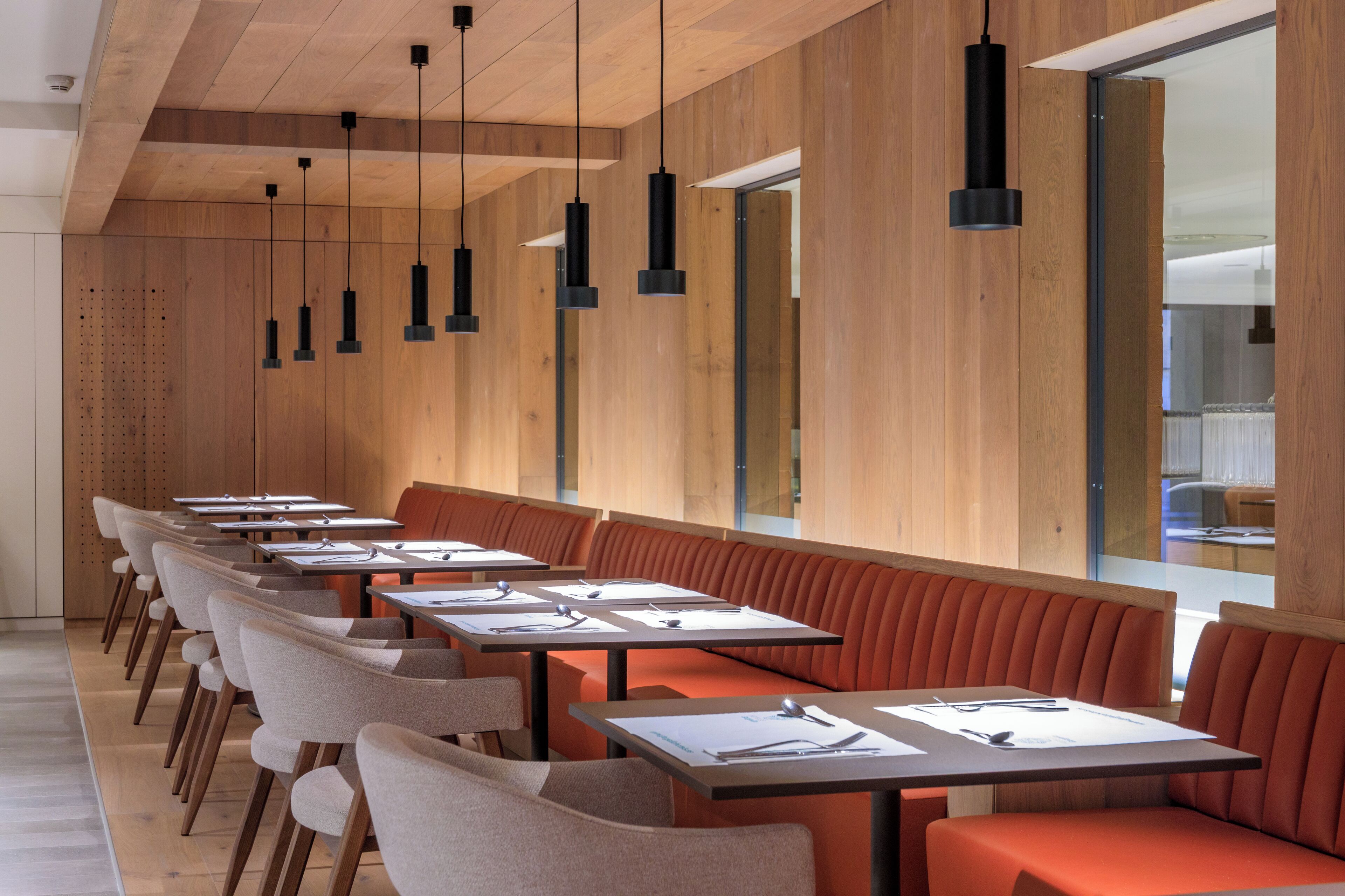 Un restaurante moderno con mesas comunitarias largas y cabinas, paredes de paneles de madera e iluminación colgante.