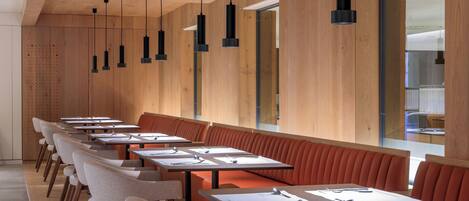 Un restaurante moderno con mesas comunitarias largas y cabinas, paredes de paneles de madera e iluminación colgante.