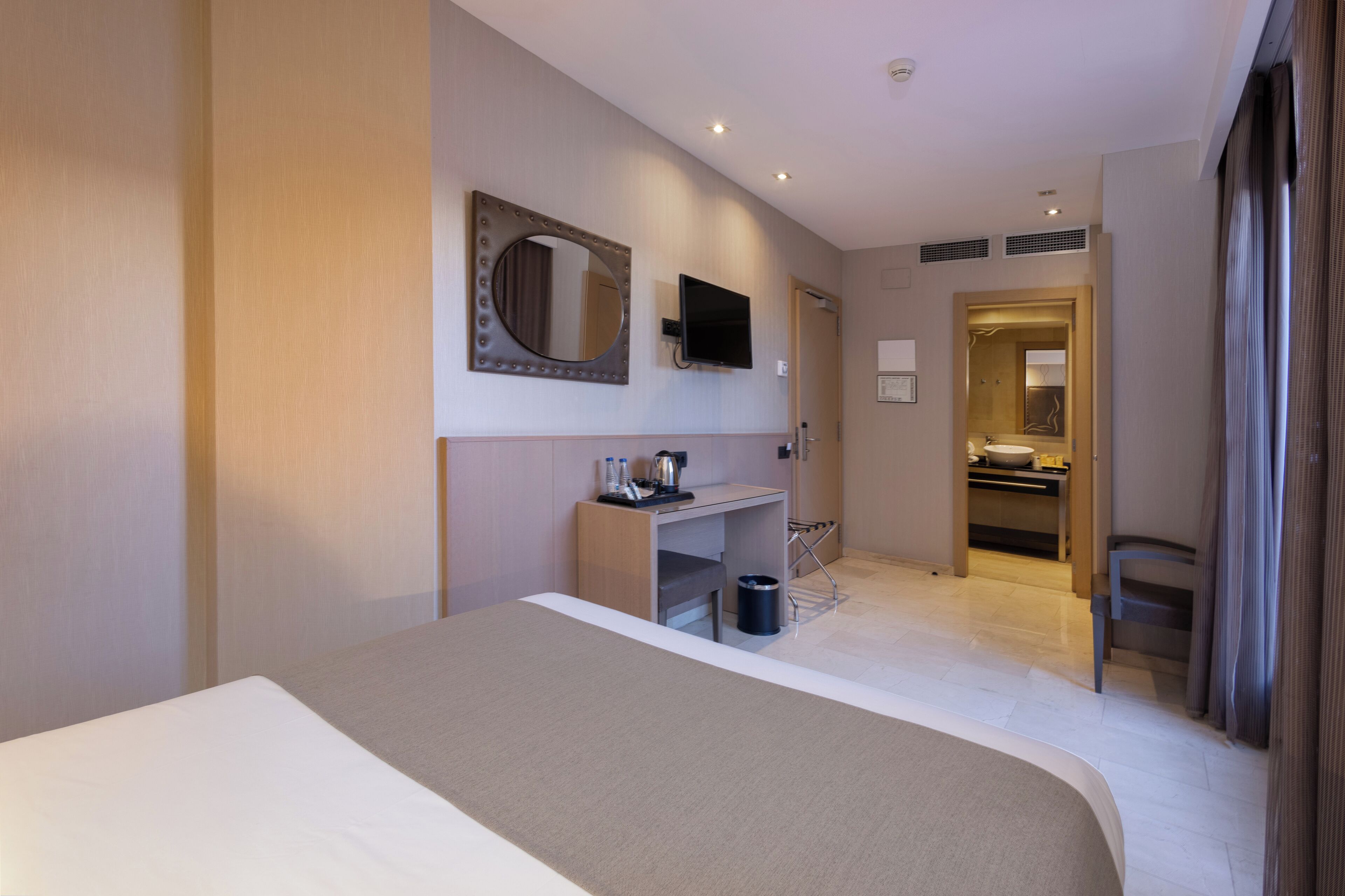 Une chambre d’hôtel avec un grand lit, un bureau doté d’un miroir, une télévision et une salle de bain visible à travers une porte ouverte.