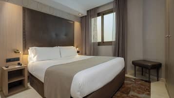 Une chambre d’hôtel moderne avec un grand lit, des tables de chevet, un petit banc et une fenêtre avec des rideaux.