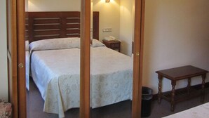 Une chambre d’hôtel avec un grand miroir, deux lits, une table de chevet, une petite table en bois et un téléviseur fixé au mur.