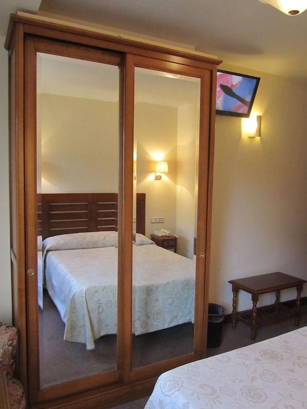 Ett hotellrum med en stor spegel, två sängar, ett sängbord, ett litet träbord och en TV som är monterad på väggen.