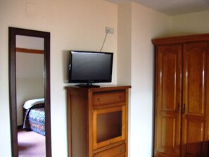 Una habitación con una televisión sobre un mueble de madera, un armario y un espejo que refleja una cama.