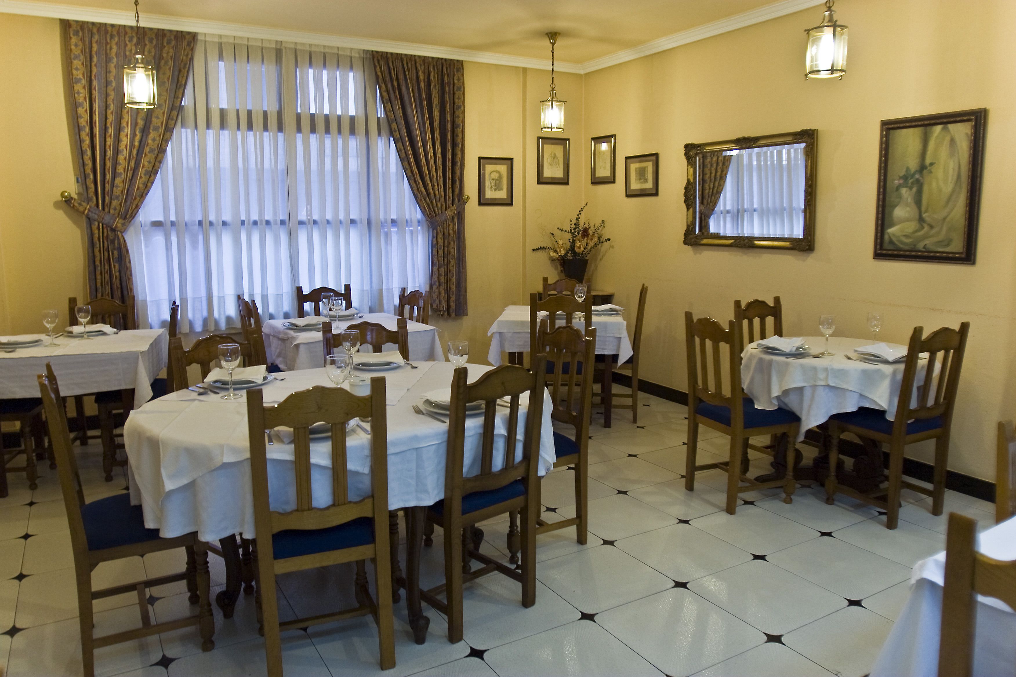 Comedor con varias mesas dispuestas para comidas, sillas de madera y una araña.