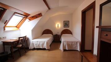 A room with two single beds, a wooden desk, a chair, a small table, and a wardrobe.