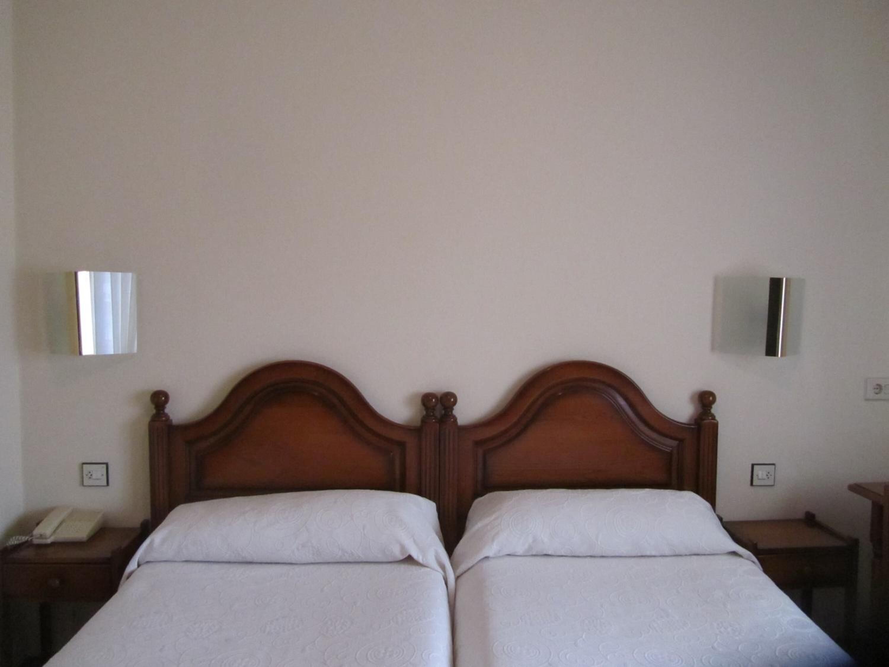 A double bed with a wooden headboard, two bedside tables, and a wall-mounted light fixture.