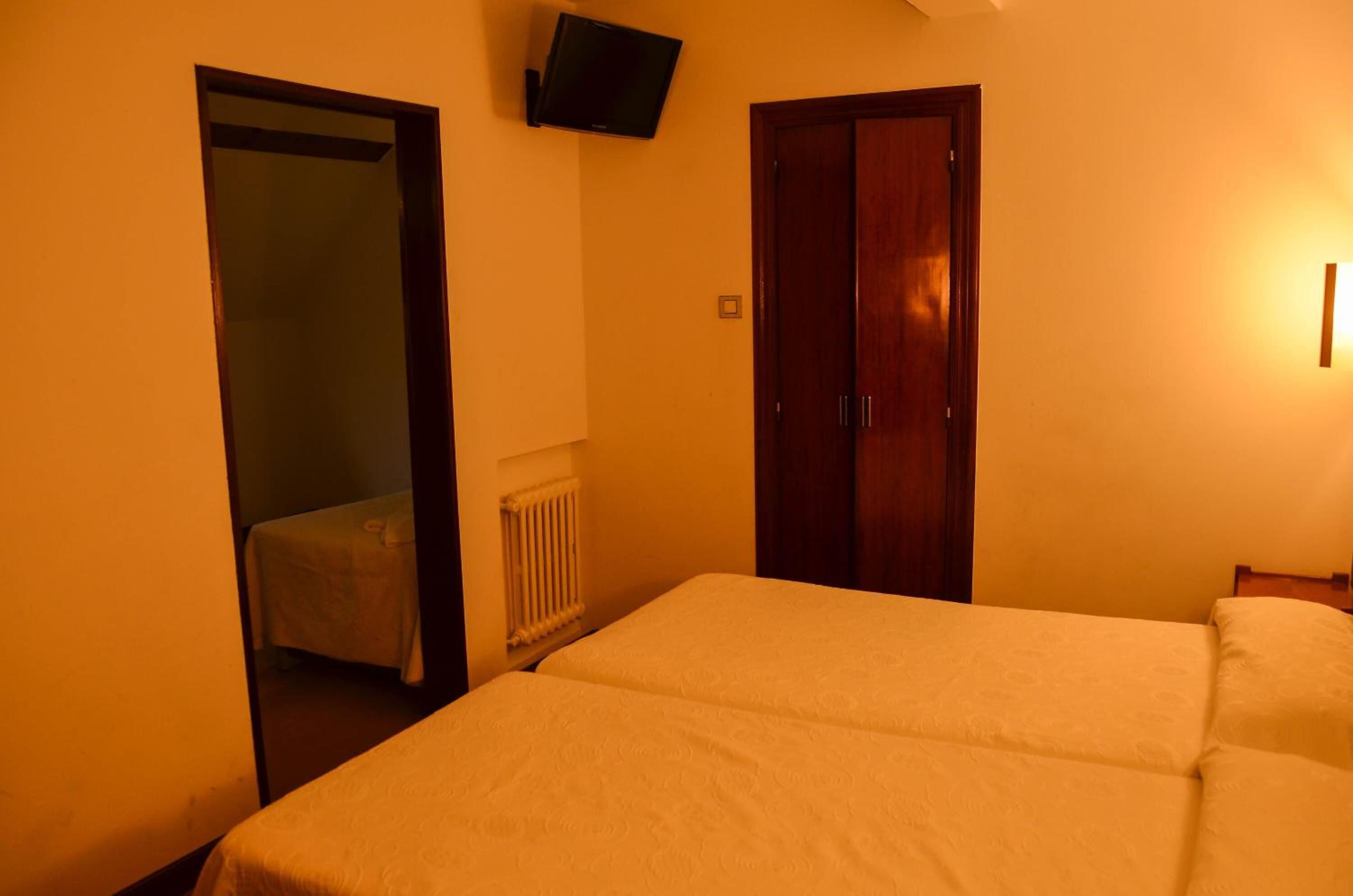 Une chambre avec deux lits, un radiateur, un téléviseur fixé au mur et une porte.