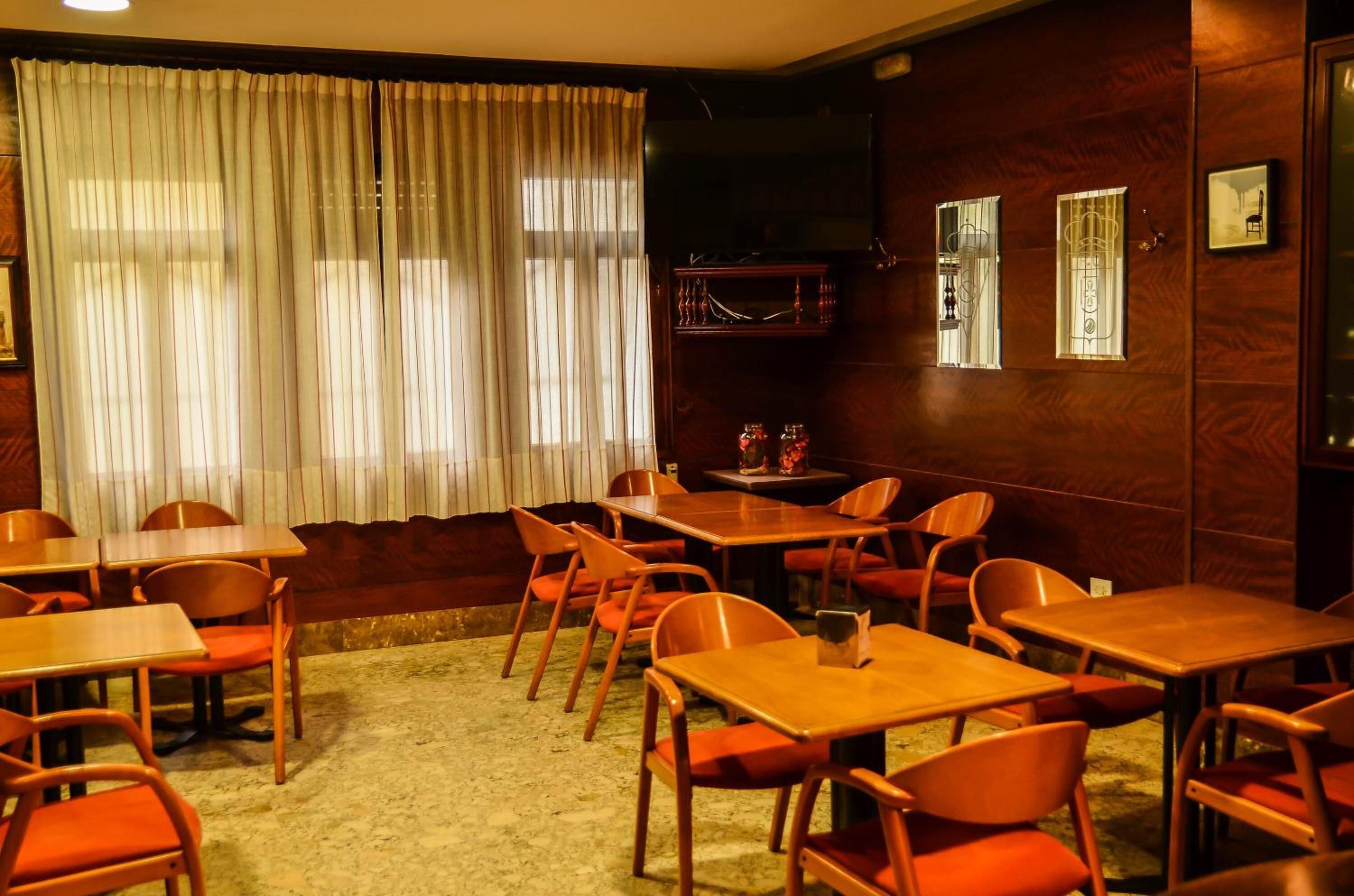 A room with wooden tables and orange chairs, a television, and a window with curtains.