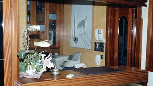 Un bureau en bois, une lampe, un arrangement floral, un tableau encadré et un téléphone.