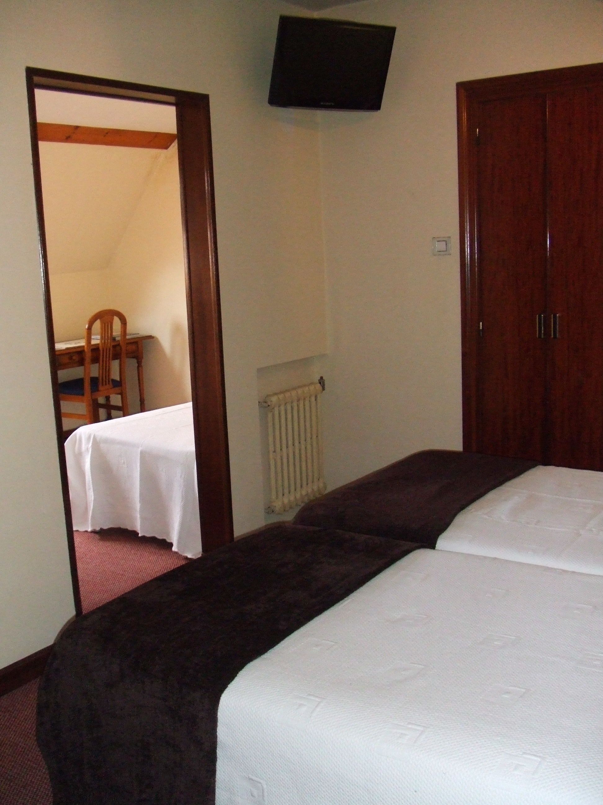 Un dormitorio con dos camas, un armario de madera, un radiador y un televisor en la pared.