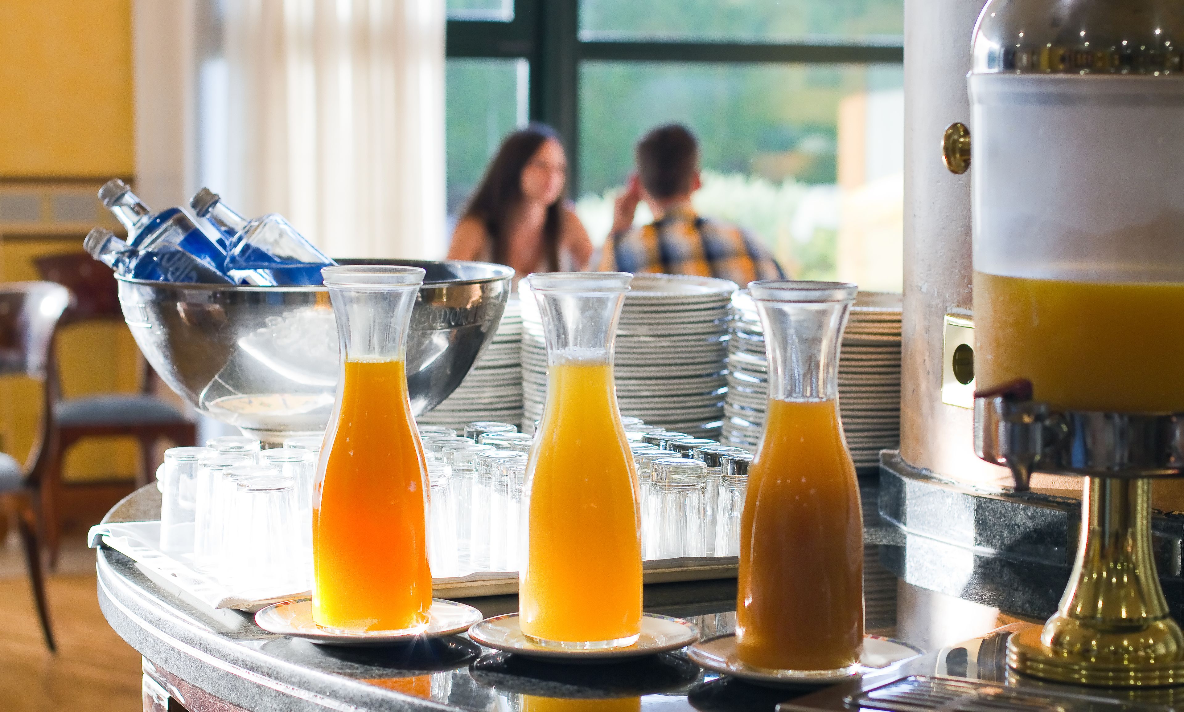 A breakfast buffet with various glass containers of orange juice and a metal pitcher.