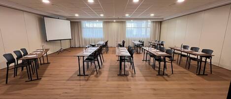A conference room with multiple tables and chairs, a whiteboard, and a projector screen.