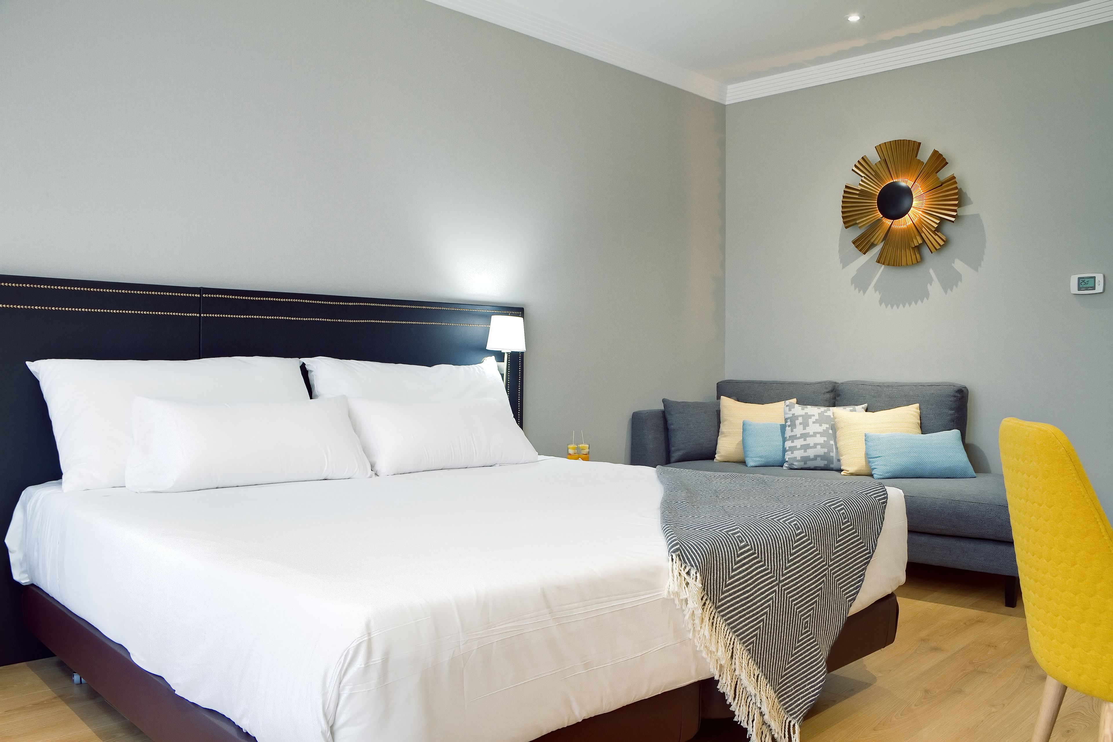 A neatly arranged bedroom with a large bed, a sofa, and a yellow chair.