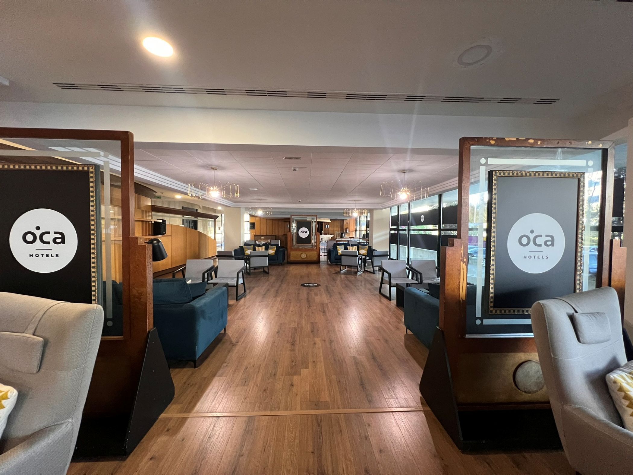 Un vestíbulo de hotel con una recepción central, zonas de estar y suelo de madera.