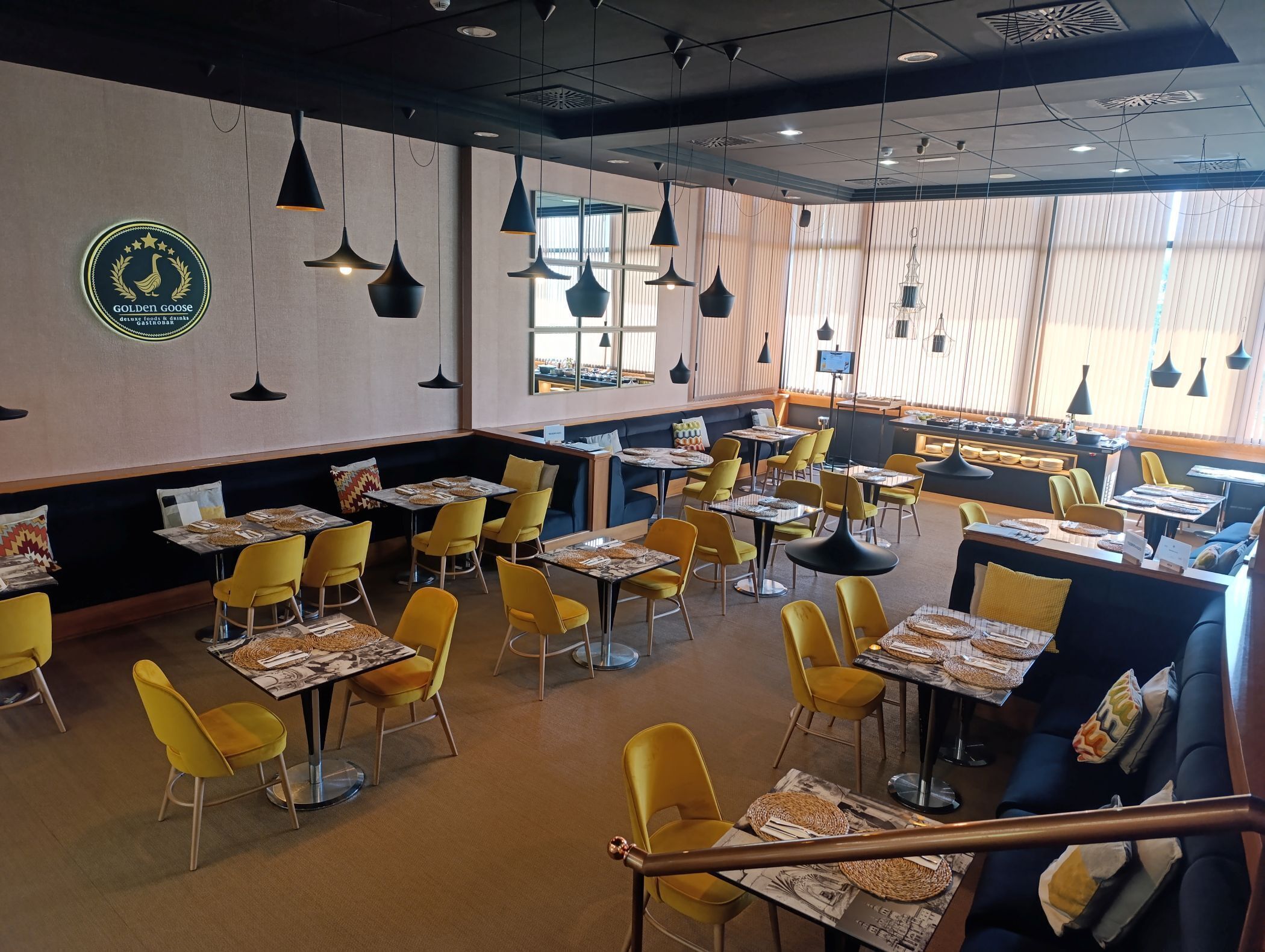 Un restaurante con sillas y mesas amarillas, un logotipo en la pared y lámparas colgantes.