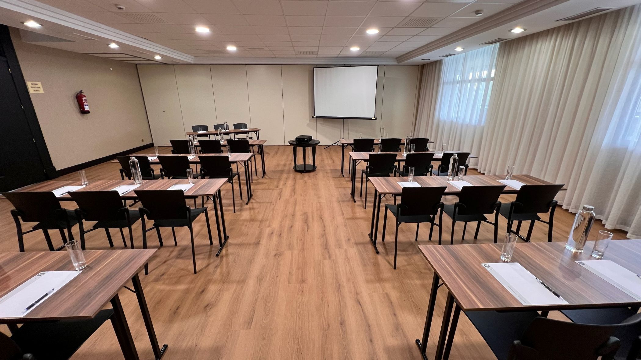 A conference room with multiple tables and chairs, a projector screen, and a fire extinguisher on the wall.