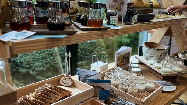 A wooden counter with various food items and condiments, including bread, jars of honey, and cheese, with a view of greenery outside. - Oca Puerta del Camino Hotel (Santiago de Compostela)