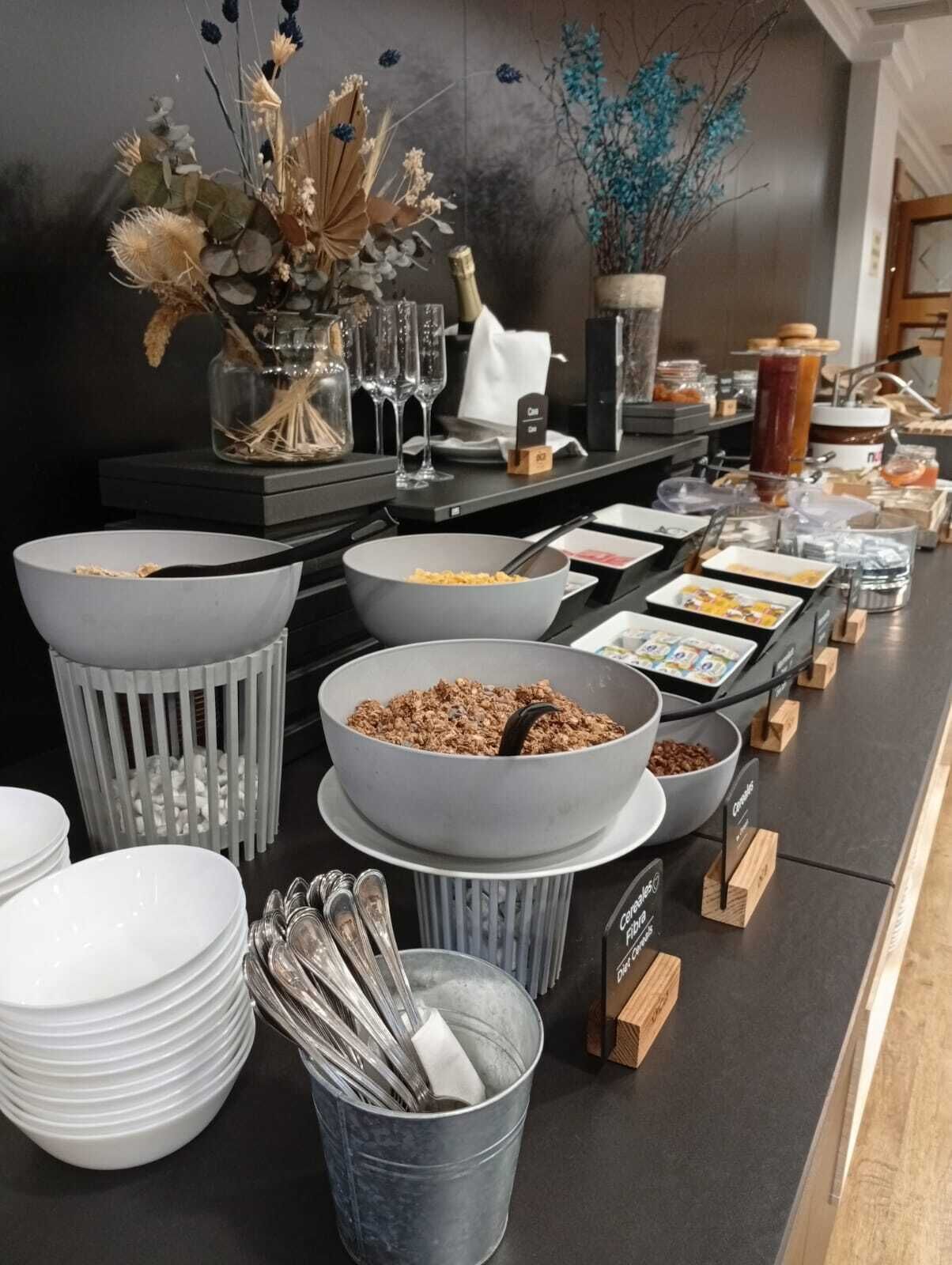 A buffet setup with various food items, including cereal and granola, and a decorative vase with dried flowers.