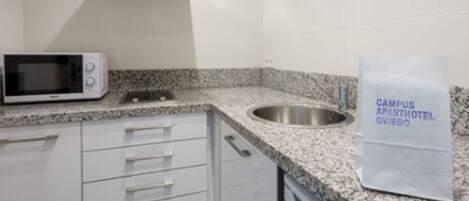 Una kitchenette con microondas, lavamanos y armarios. Un letrero en la pared dice "CAMPUS APARTHOTEL OVIDO".
