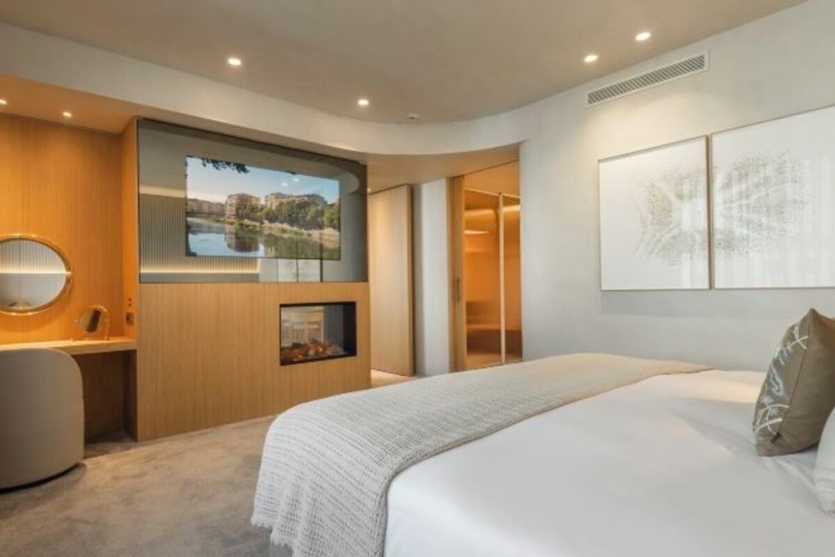 A modern hotel room with a large bed, a desk, a television, and artwork on the walls.