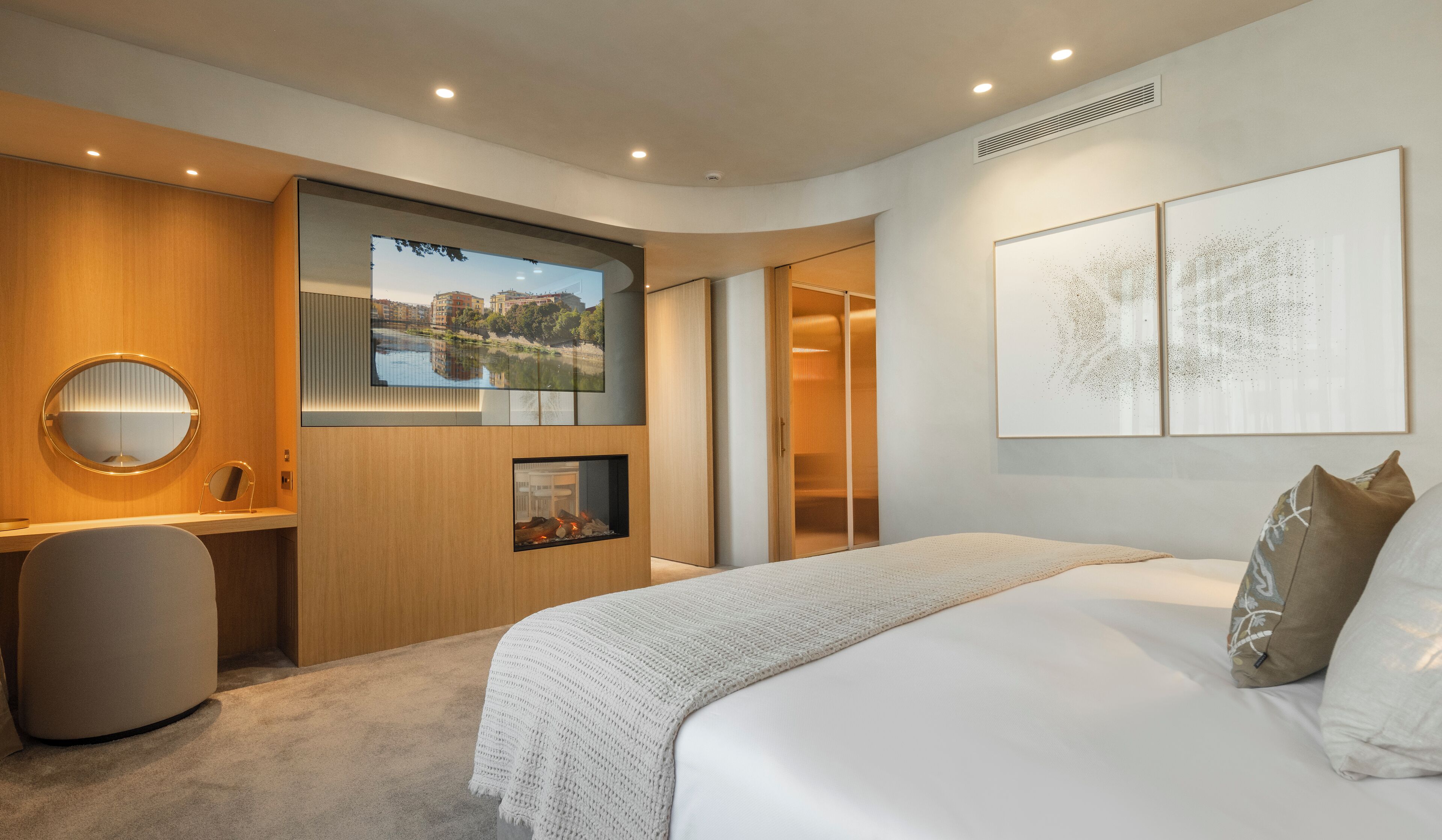 A modern hotel room with a large bed, a desk with a computer, a TV displaying a cityscape, and artwork on the wall.