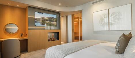 A modern hotel room with a large bed, a desk with a computer, a TV displaying a cityscape, and artwork on the wall.