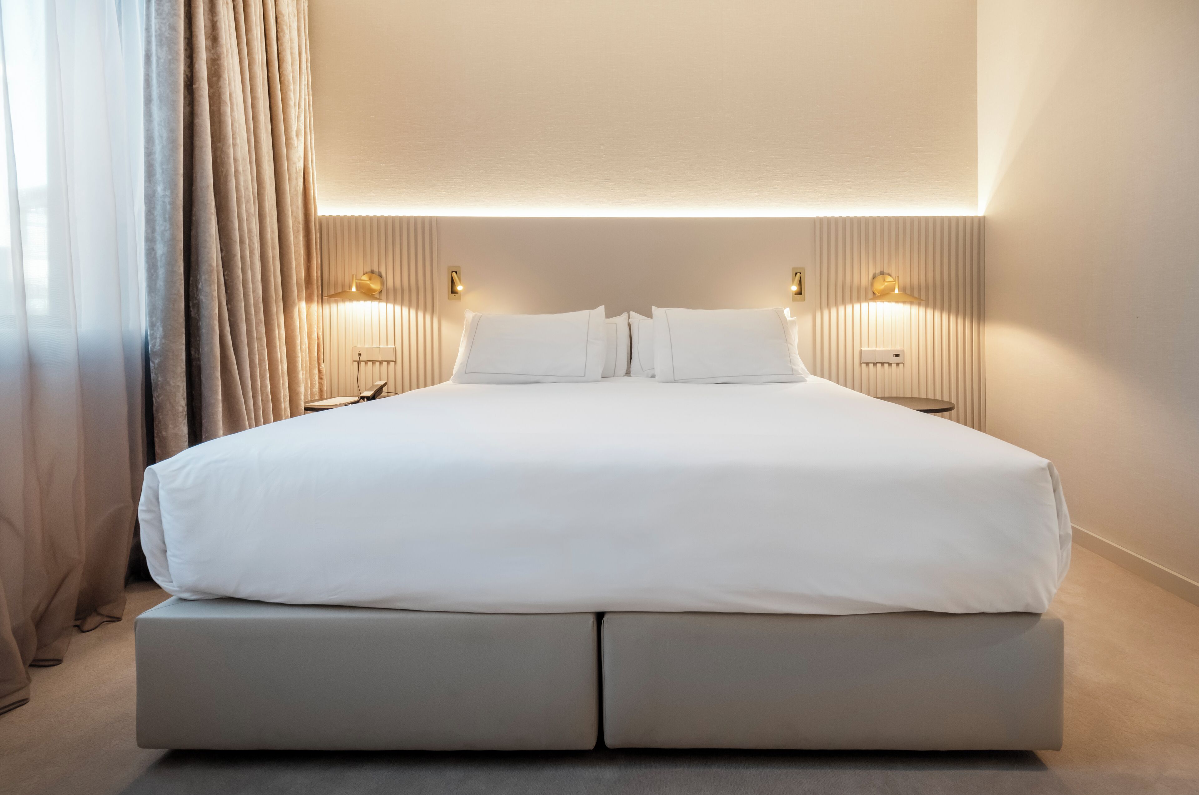 Une chambre d’hôtel moderne avec un grand lit, deux tables de chevet et un luminaire fixé au mur.