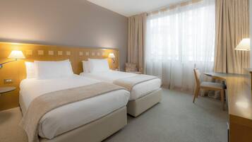 Habitación de hotel con dos camas, un escritorio, una silla y un ventanal con cortinas.
