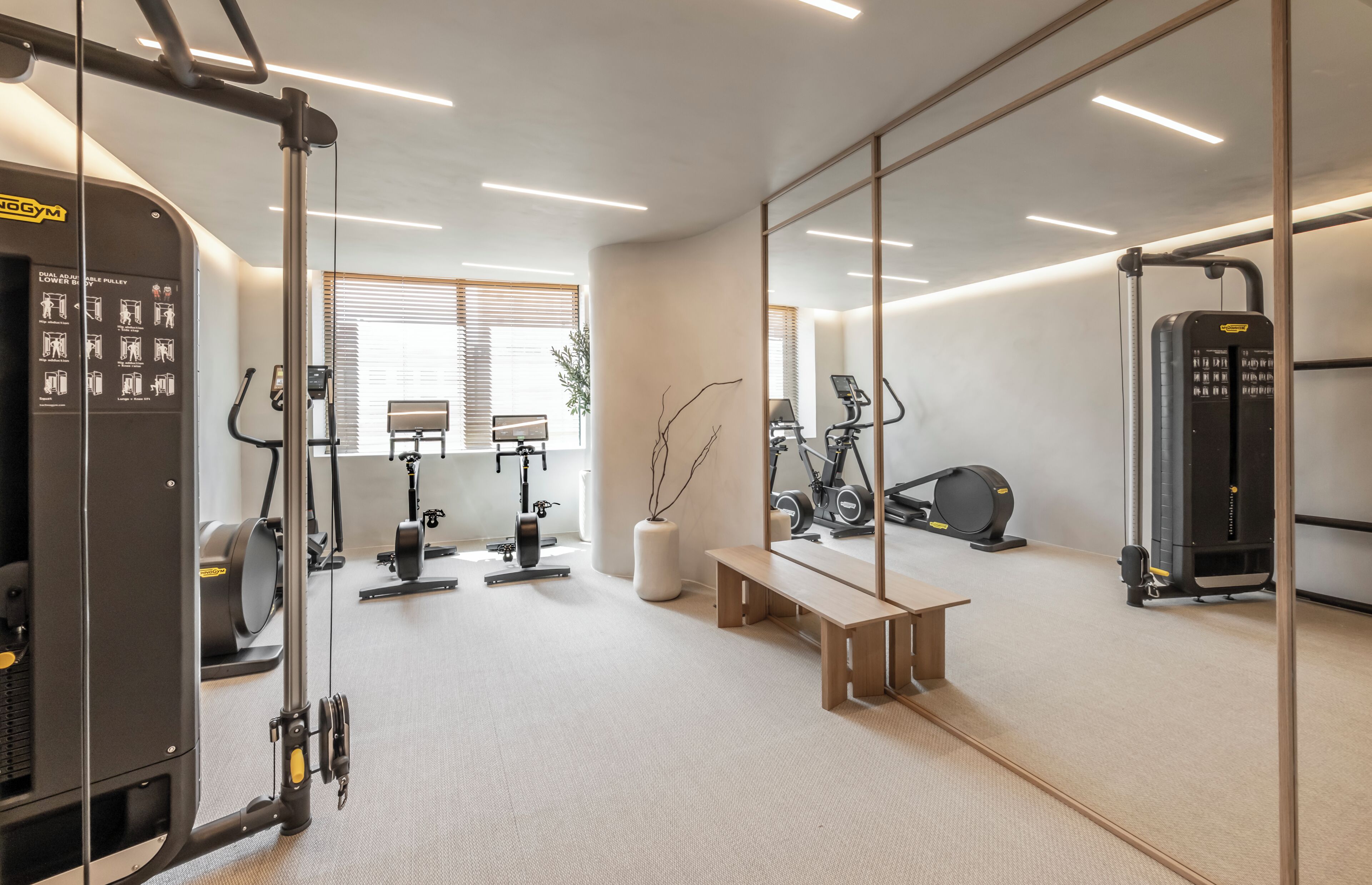 A modern gym with various exercise equipment, a mirrored wall, and a bench.