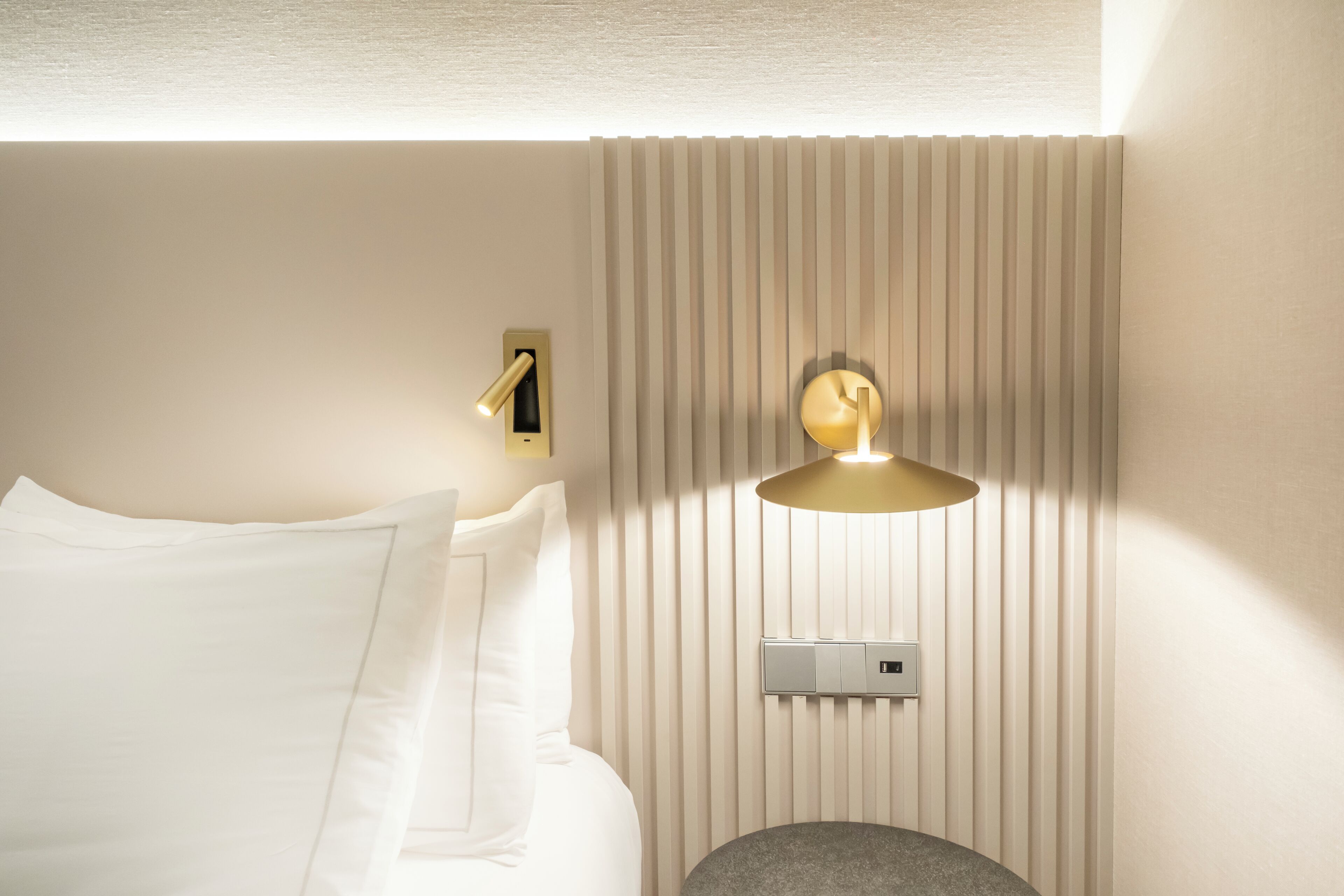 A hotel room with a bed, a wall-mounted thermostat, and a wall-mounted light fixture.