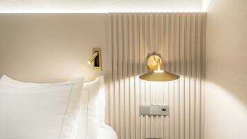 A hotel room with a bed, a wall-mounted thermostat, and a wall-mounted light fixture.