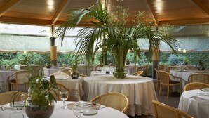 Un restaurante con mesas redondas, sillas de mimbre y plantas en macetas.