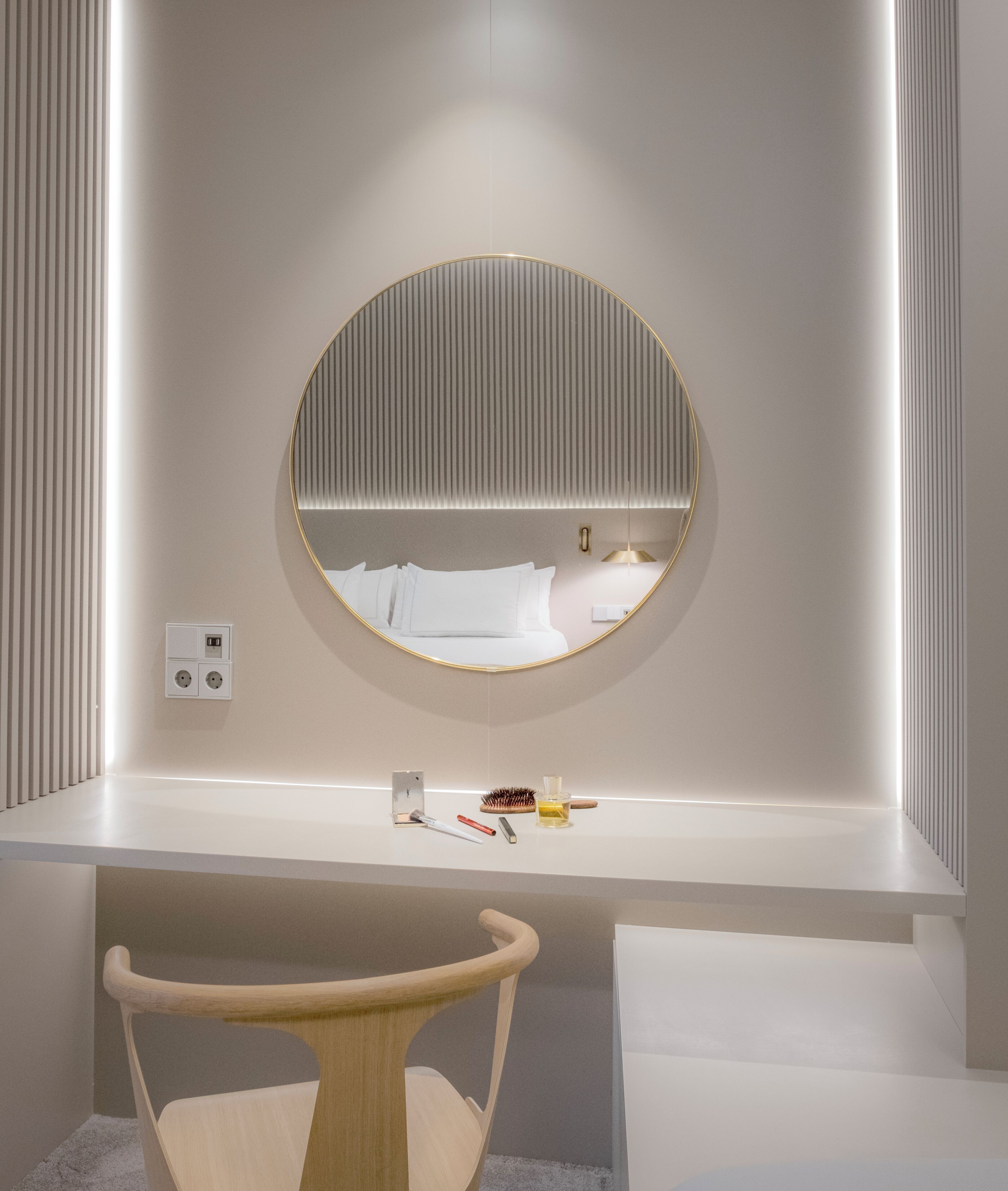Un baño moderno con un espejo redondo, un tocador blanco y una silla de madera.