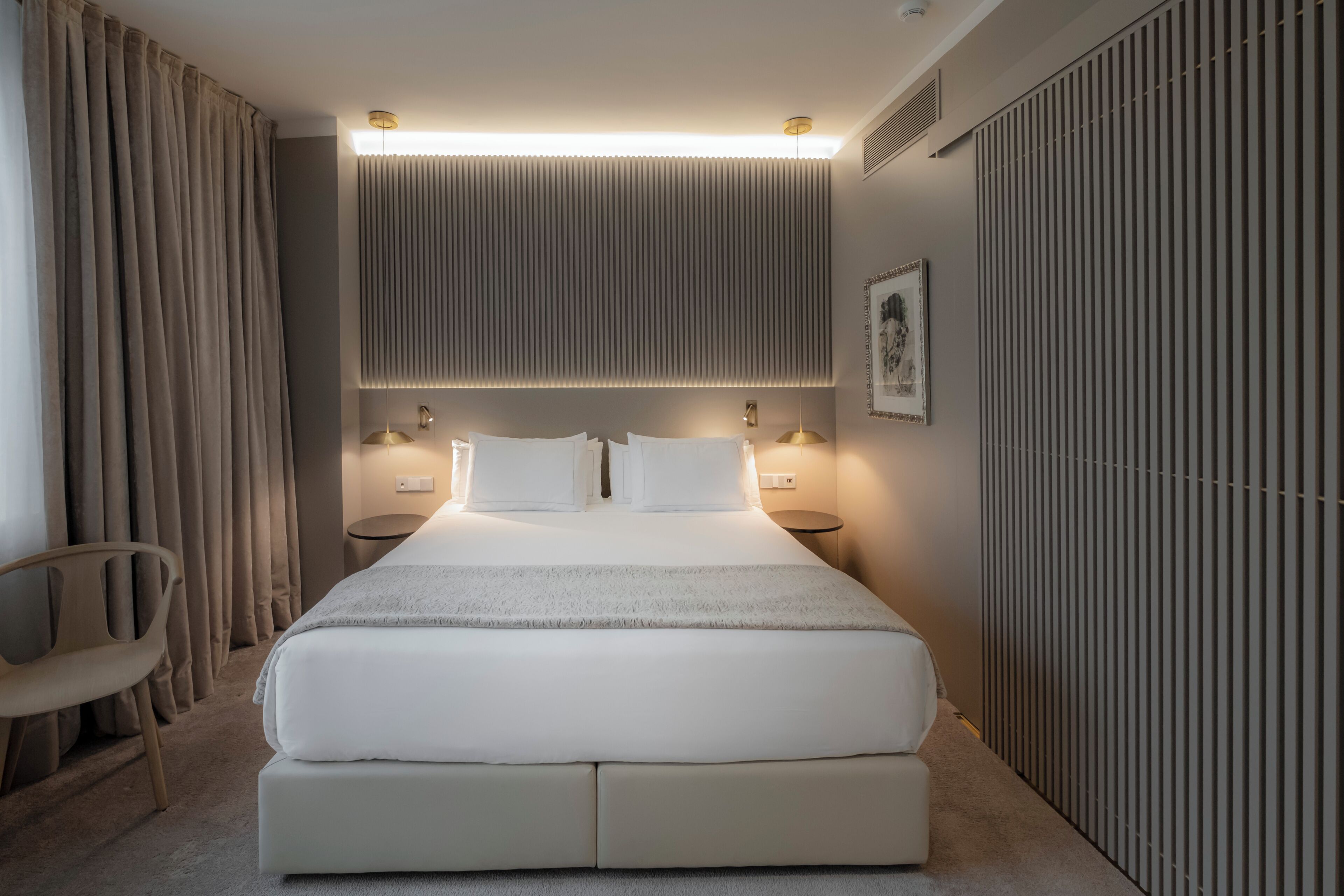 Una habitación de hotel moderna con una cama grande, lámparas de noche, una silla y un radiador.