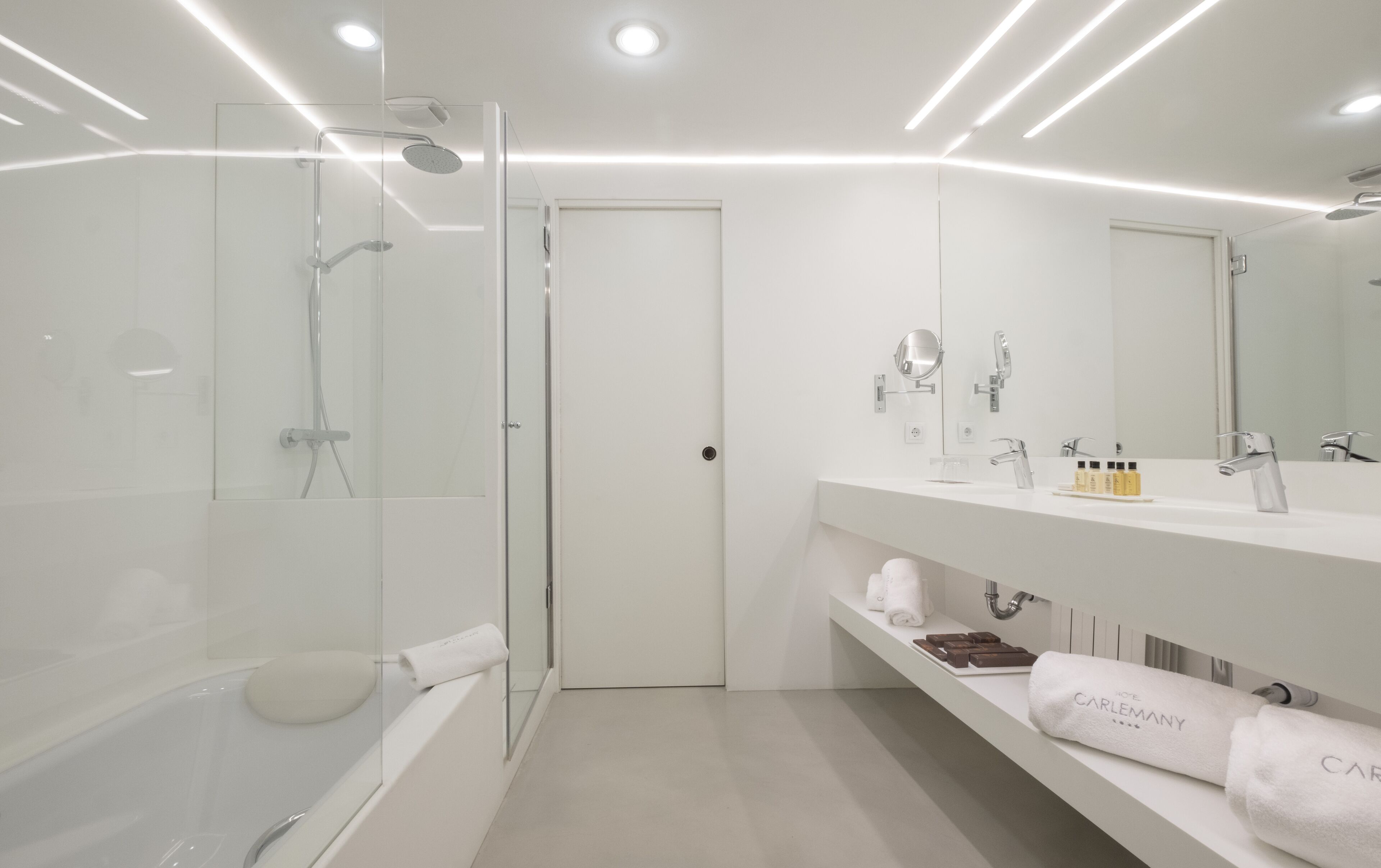 Une salle de bain moderne avec une douche à parois de verre, un meuble-lavabo blanc avec un miroir et une porte donnant sur une autre pièce.