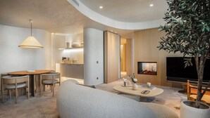 Una sala de estar moderna con un sofá, una mesa de centro y un comedor con una mesa y sillas. Hay un televisor montado en la pared y una planta en maceta en la esquina.