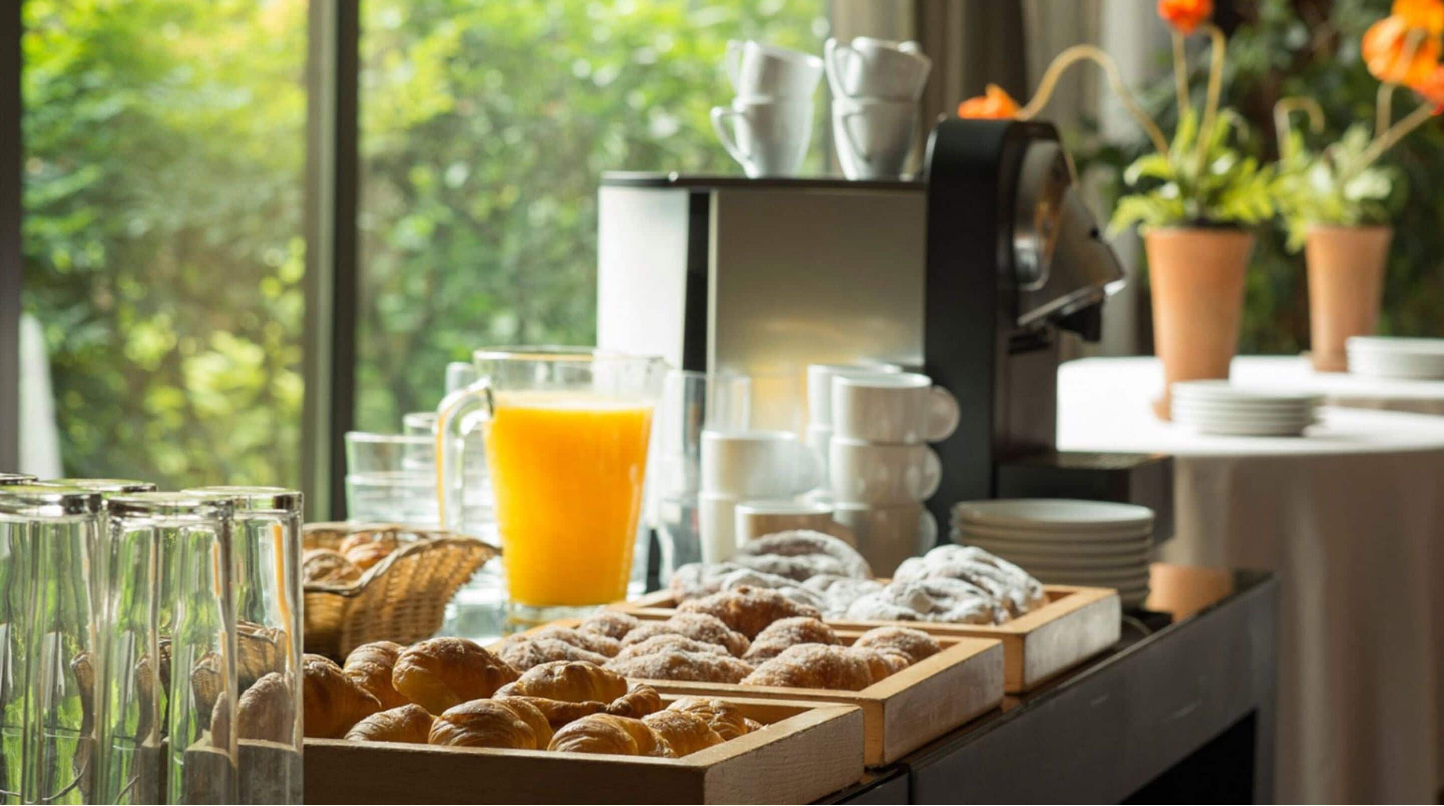 En morgenmadsbuffet med bagværk, en kaffemaskine og et glas appelsinjuice.
