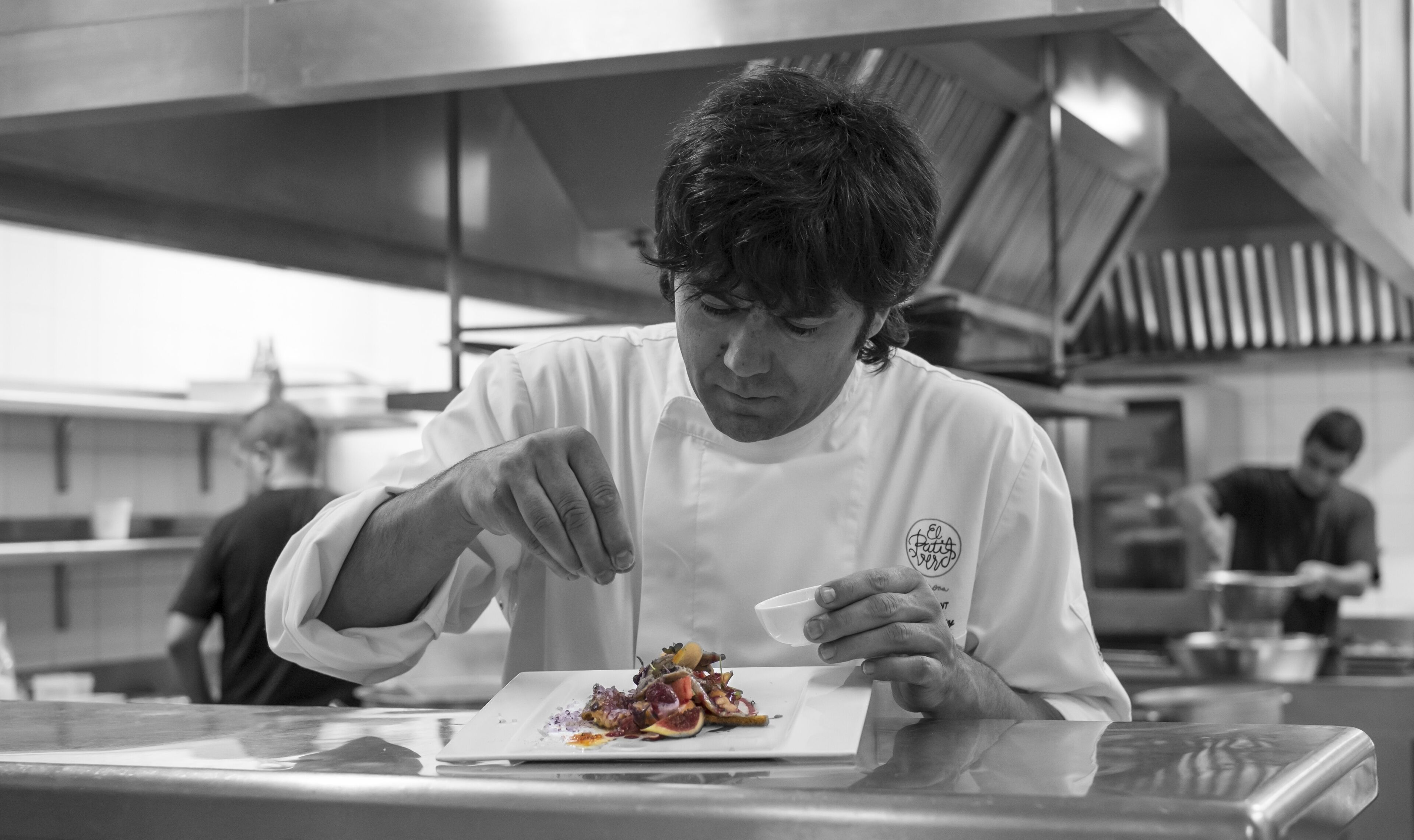 Un chef preparando un plato en una cocina profesional con superficies de acero inoxidable y equipo moderno.