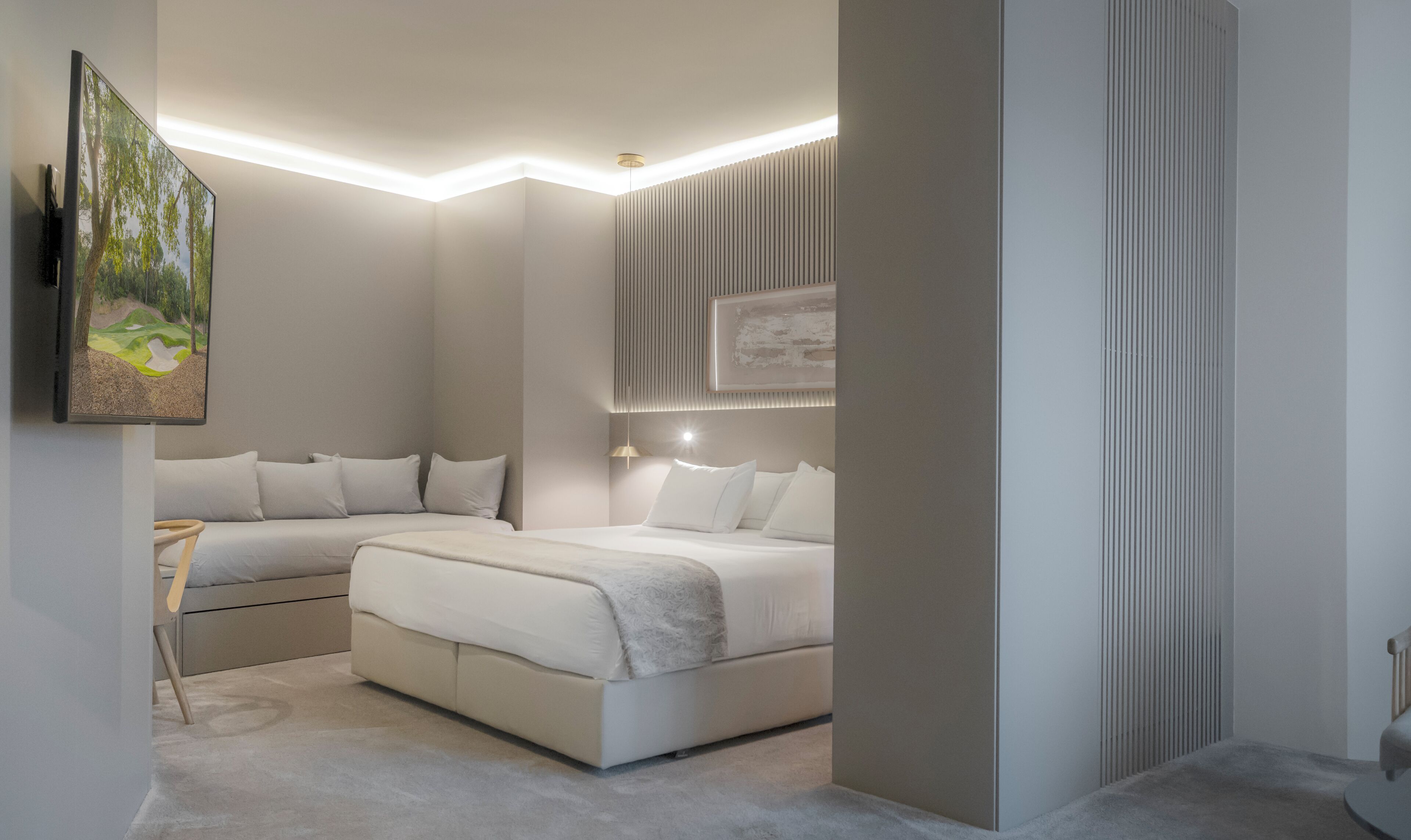 Un dormitorio moderno con una cama grande, un sofá más pequeño y un televisor montado en la pared.