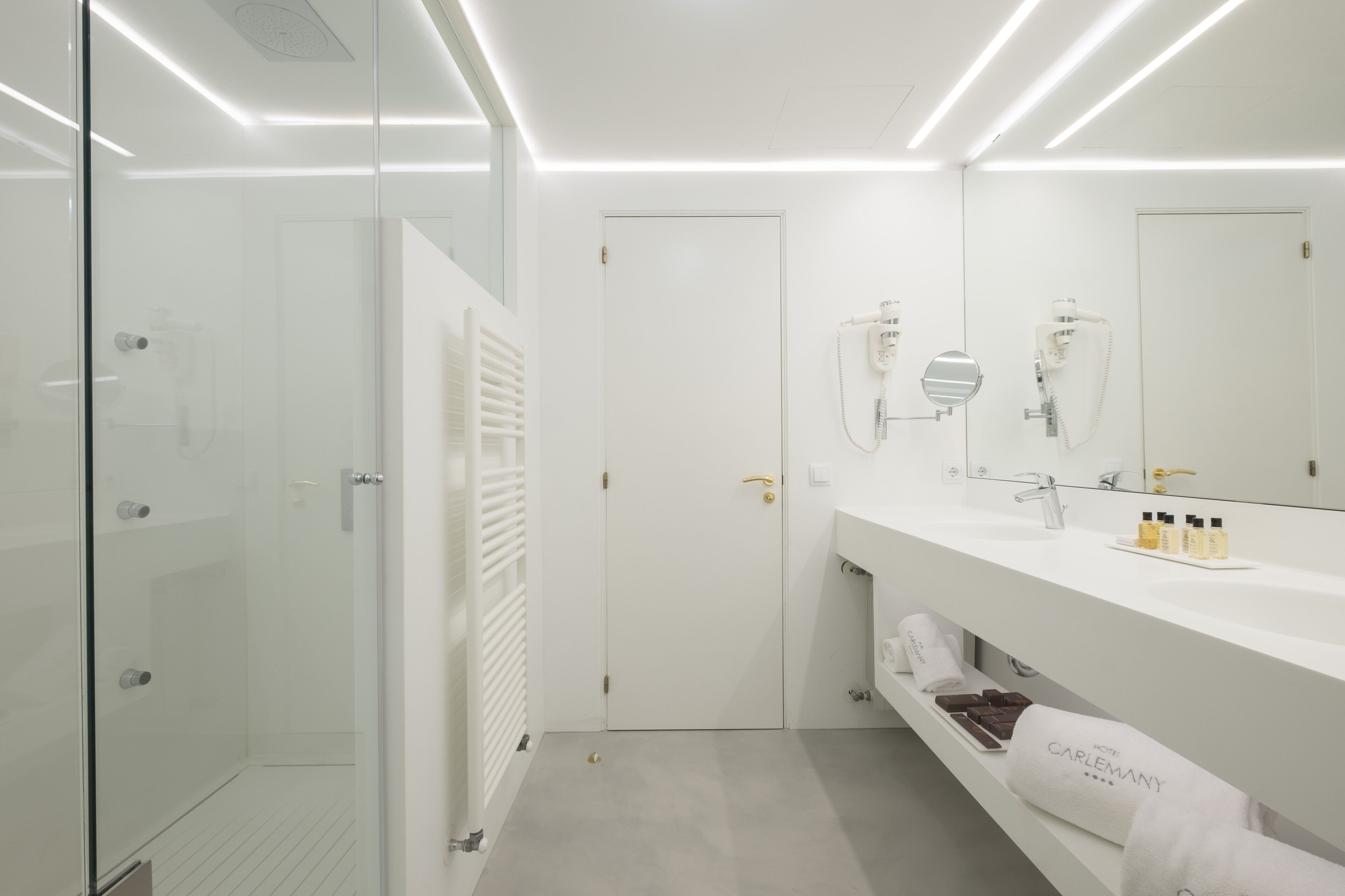 Une salle de bain moderne avec une douche à parois de verre, un meuble-lavabo blanc avec un miroir et un porte-serviettes orn é d’une serviette de marque.