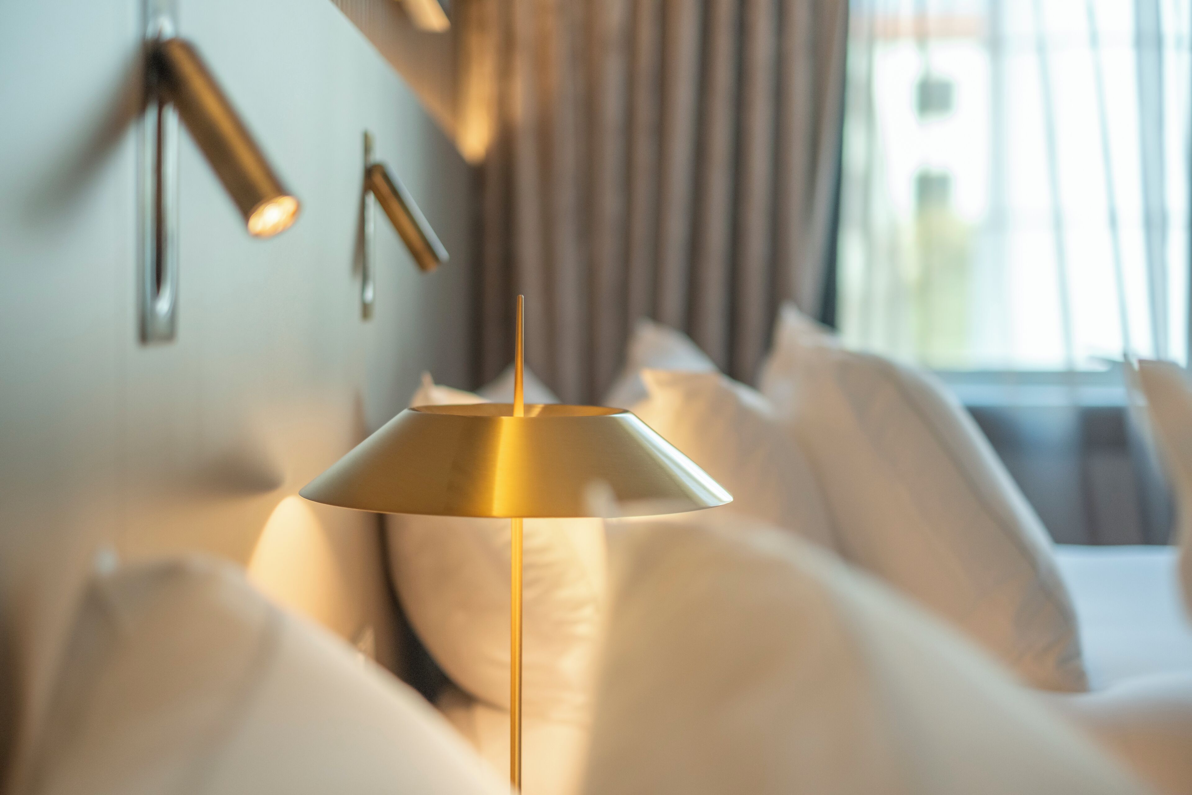 A modern bedroom with a bed, a wall-mounted lamp, and a window with curtains.