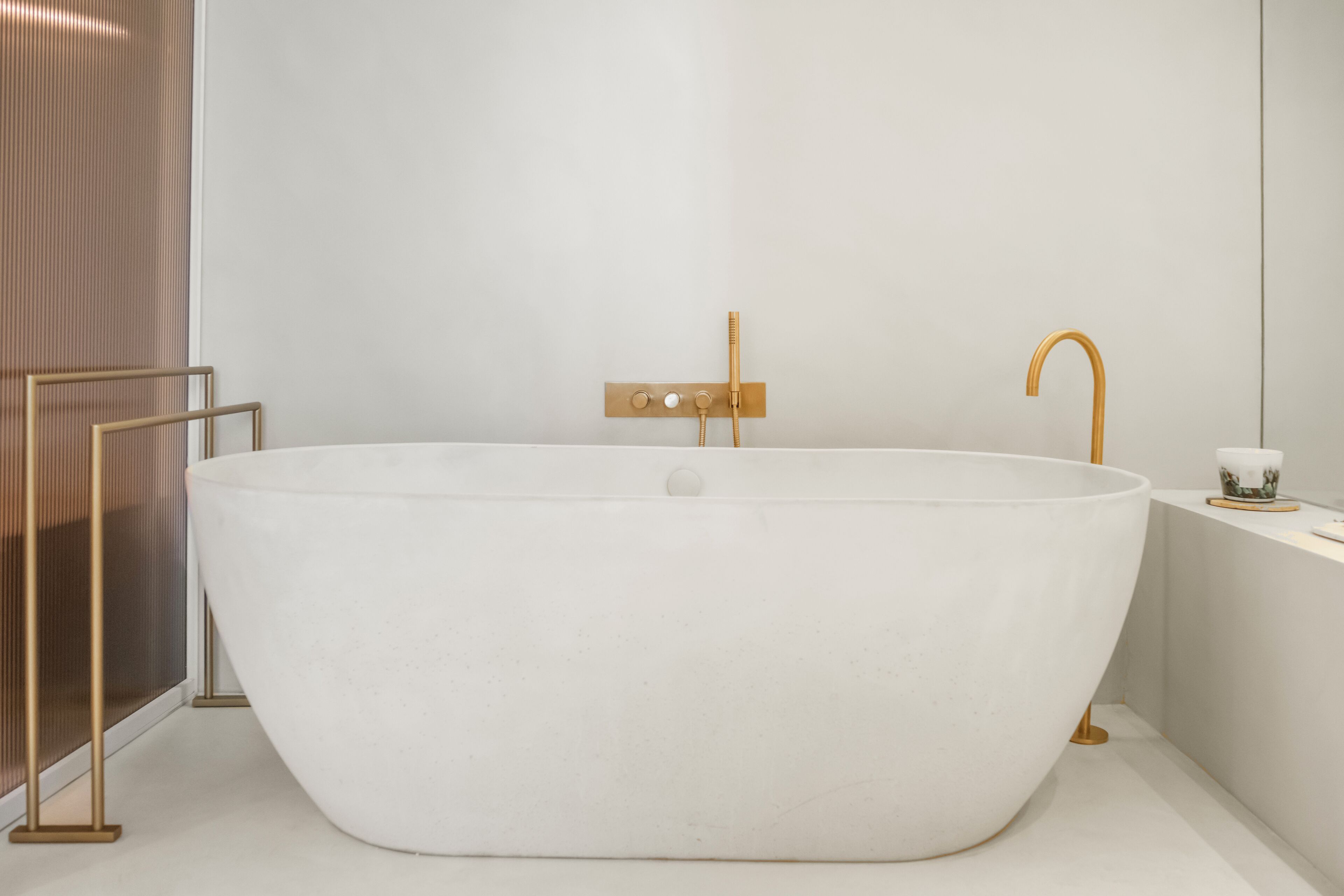 Una bañera independiente en un baño de diseño minimalista, un perchero y una mesita con una taza.
