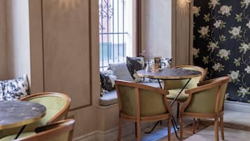 A cozy seating area with a round table and chairs, a window with decorative iron bars, and a floral wallpaper.